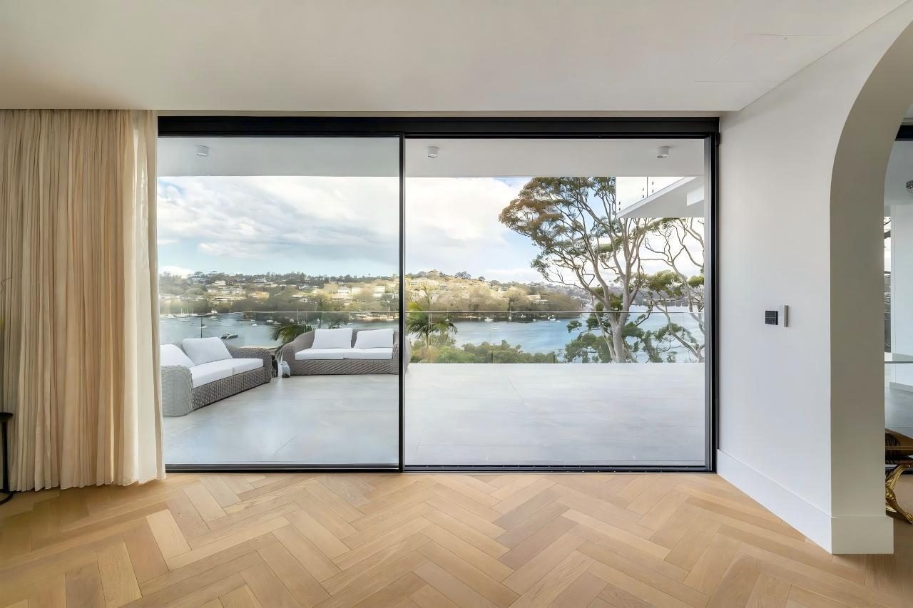 Slimline sliding glazing opening to a waterfront terrace with herringbone flooring